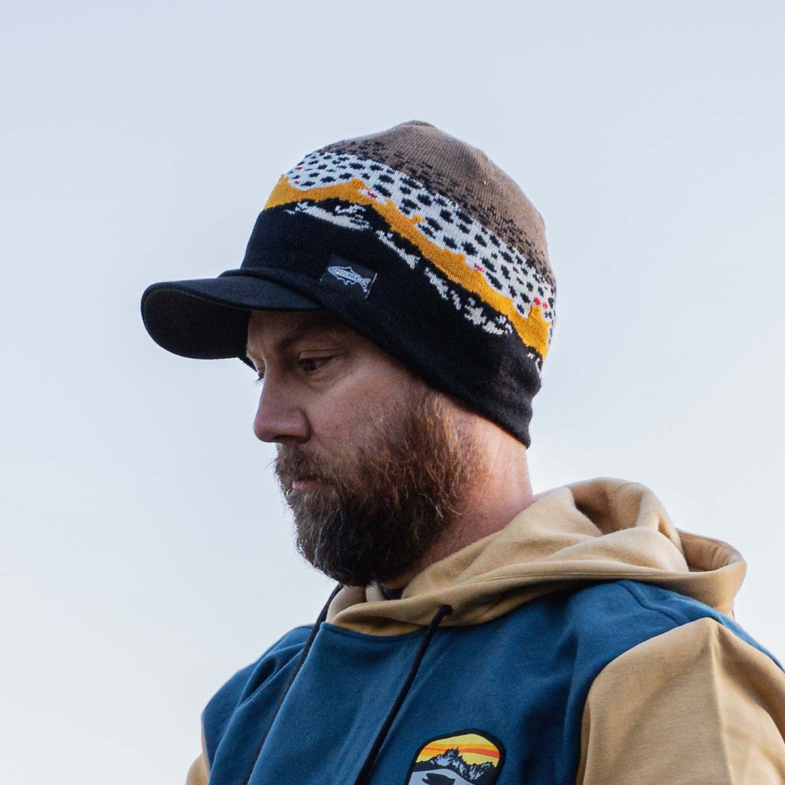 man wearing beanie skullcap with black mountains and brown trout pattern sunset 