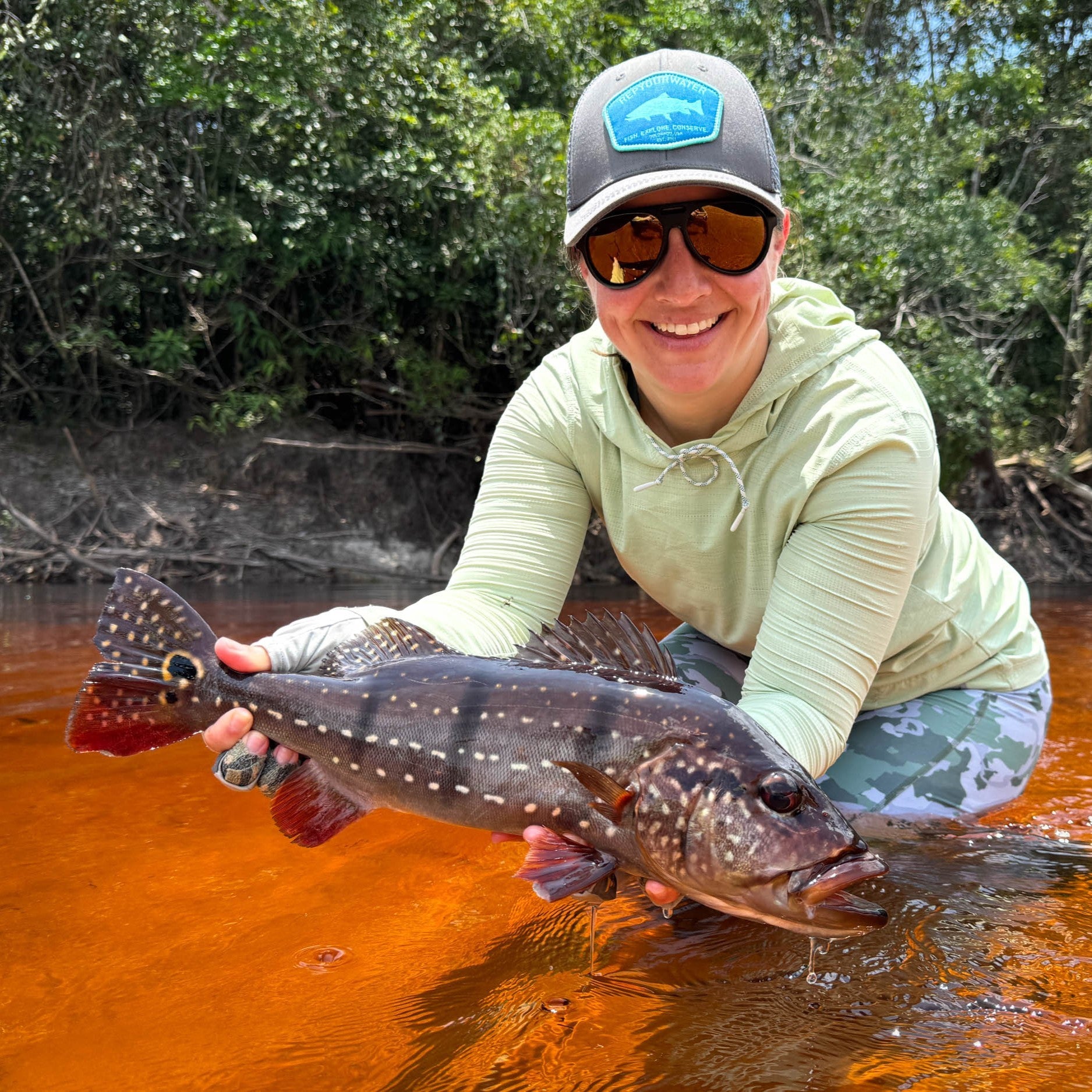 Corinne holding a peacock bass wearing a flolite sun hoody