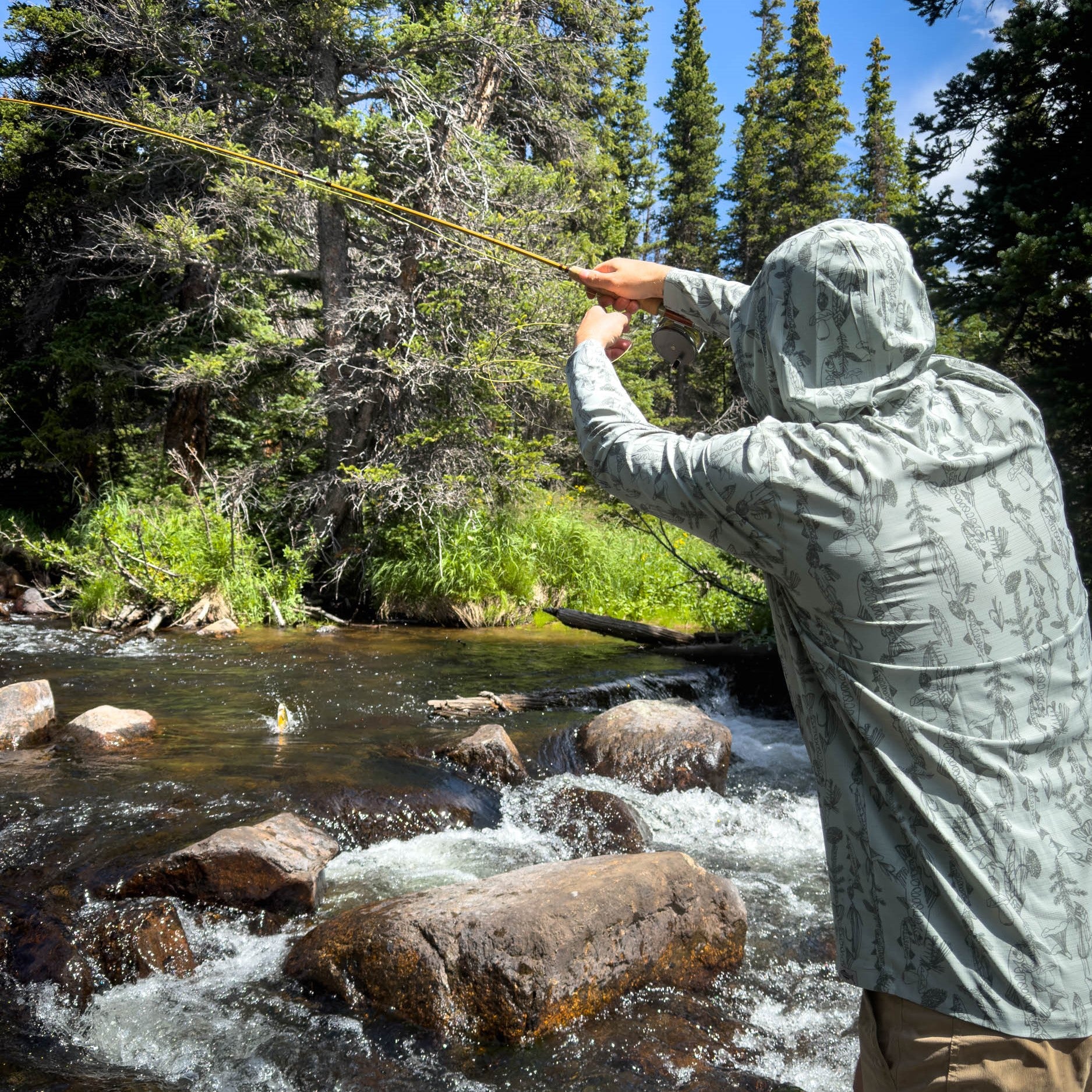 man hooked into a brook trout wearing spring forest flolite sun hoody