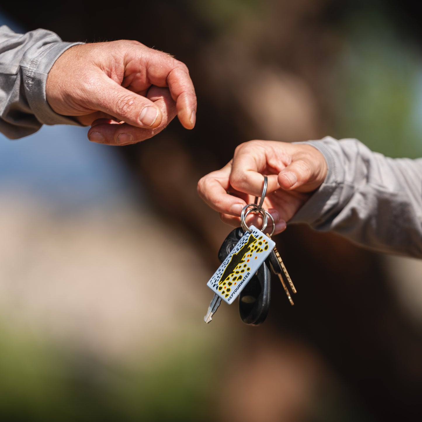 two hands passing a set of keys with the repyourwater brown trout flank key chain