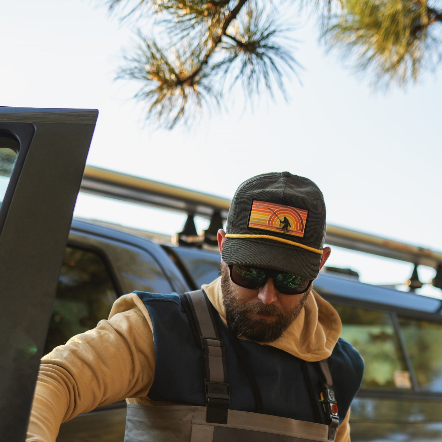 man getting out of truck with green corduroy hat n with a patch of sasquatch fishing at sunset with a retro look
