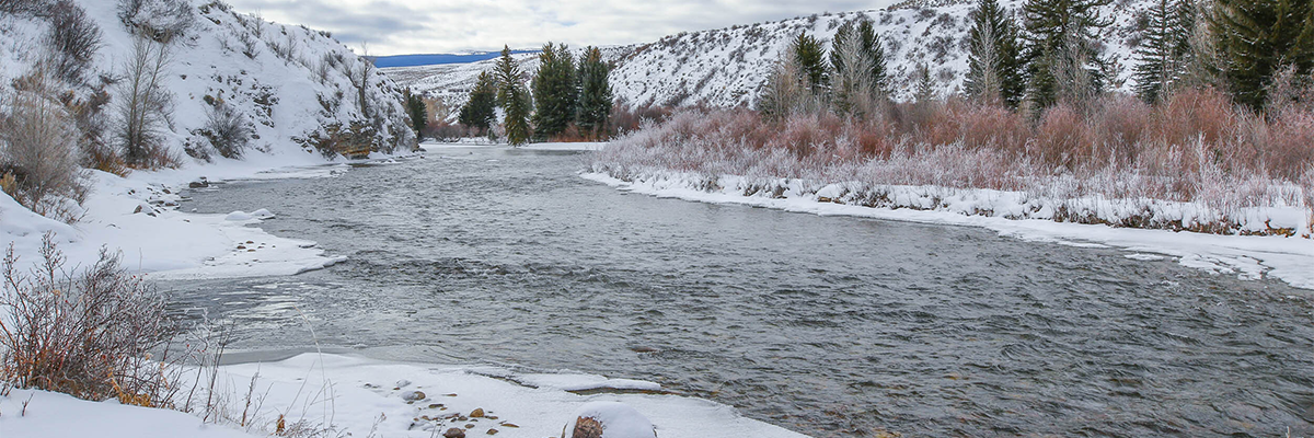 Snow covered landscape with river running through and mountains in the background