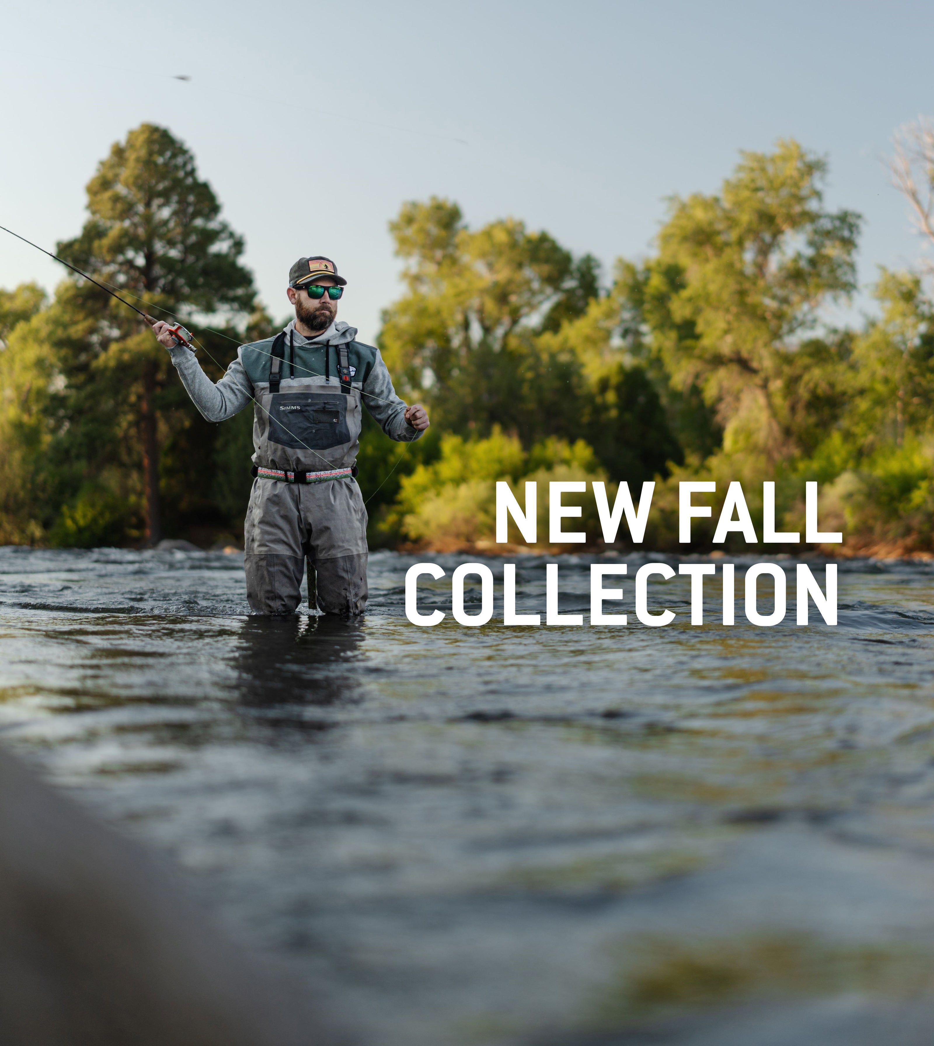 Man standing in river with fly fishing rod in waders, sweatshirt, hat and sunglasses